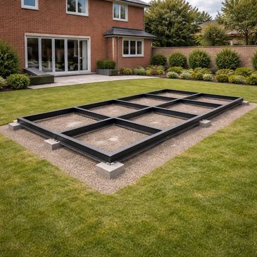 Metal frame foundation set in a backyard near a house, likely for a garden structure.