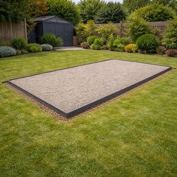 A rectangular gravel area in a green garden with shrubs and a shed.