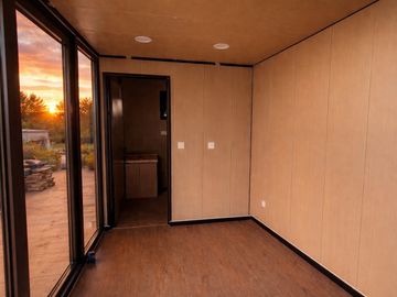 Empty room with large glass doors and wooden walls at sunset.