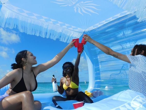 Friends cheering with red cups on a boat under a blue sky.