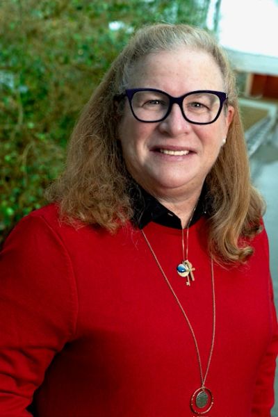 Smiling woman with glasses wearing a red sweater outdoors.