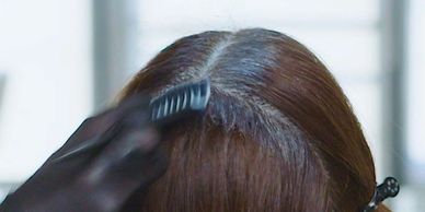 A gloved hand combing a woman's parted hair at the scalp.
