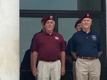 Two men in berets and polo shirts standing on steps.
