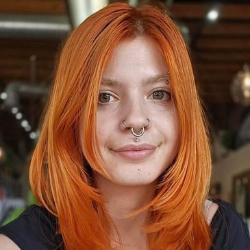 Young woman with bright orange hair and facial piercings.
