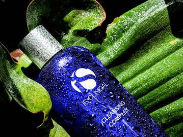 Blue cleansing complex bottle with water droplets on green leaves.