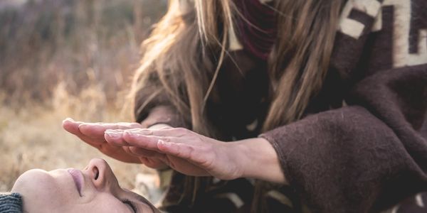 A person placing hands above another person's face outdoors.