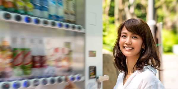 Smiling woman standing next to a vending machine outdoors.
