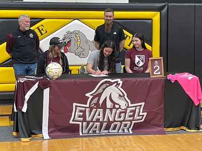 Young athlete signs with Evangel University surrounded by supporters in a gym.