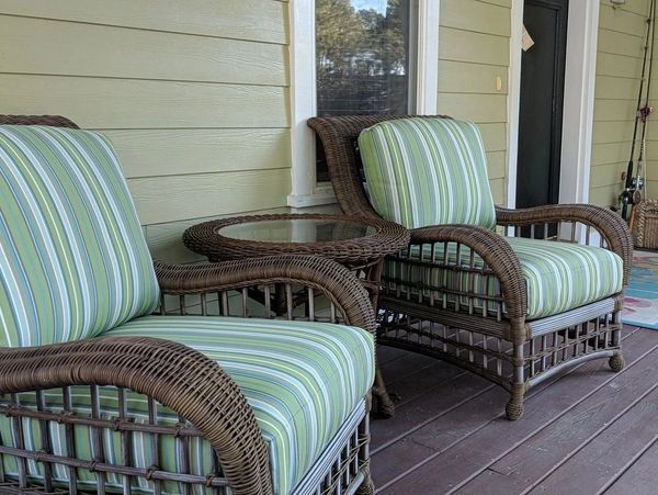 Two wicker chairs with striped cushions and a glass-top table on a porch.
