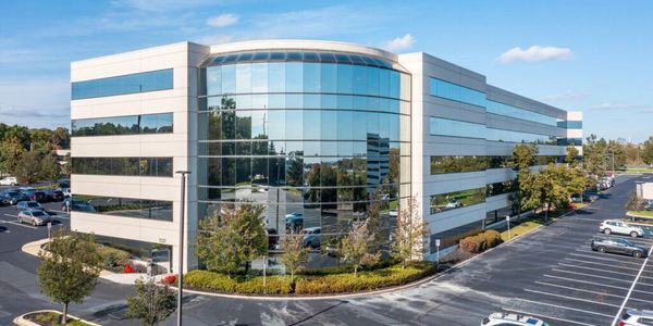 Modern office building with reflective glass windows and surrounding parking lot.