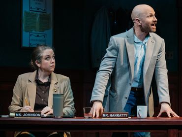 Two people in a courtroom setting appearing serious and engaged.