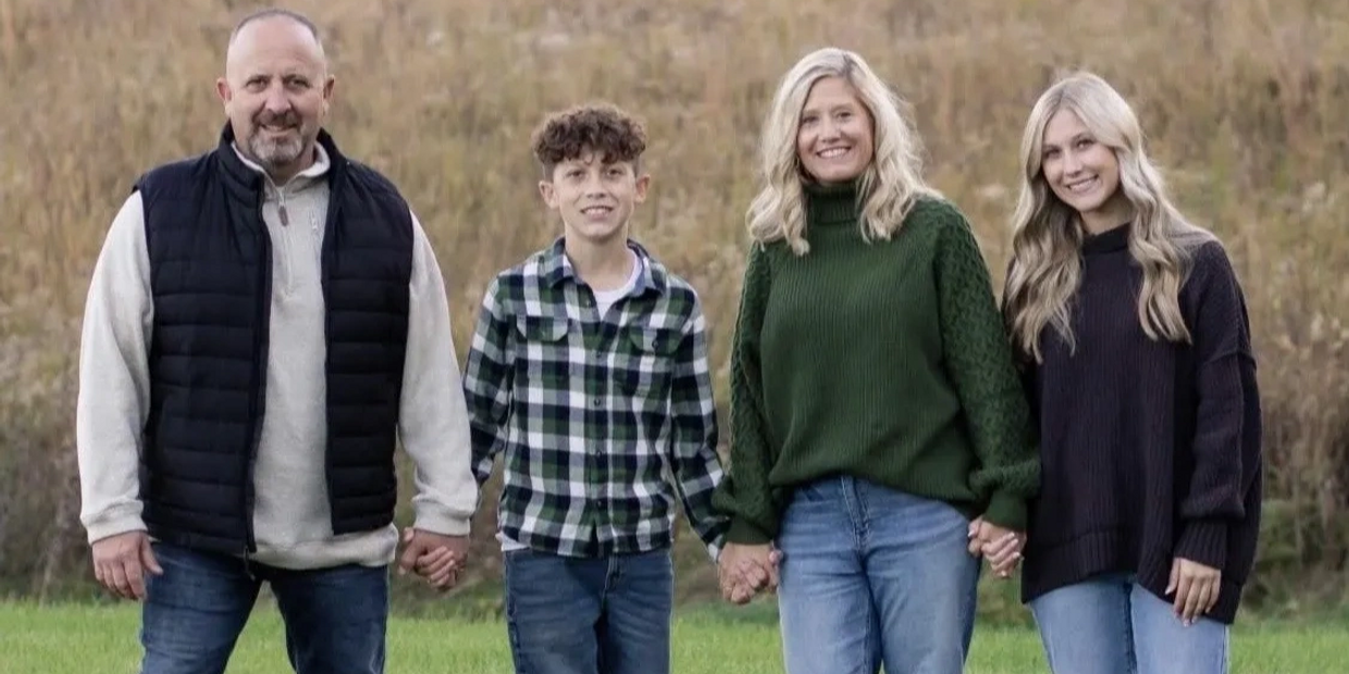 A family of four holding hands outdoors, smiling at the camera.