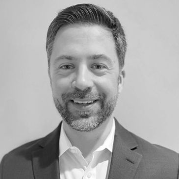Smiling man in a suit with a beard posing against a plain background.