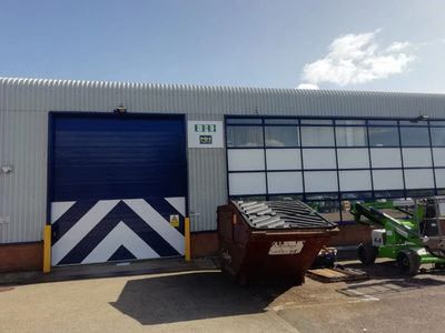 Industrial building with a large blue and white door and a dumpster outside.
