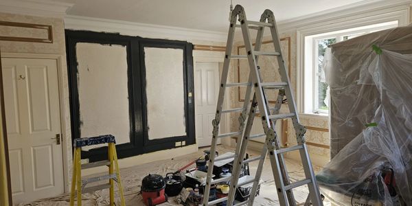 Room undergoing renovation with ladders and covered furniture.