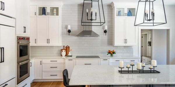 Modern white kitchen with marble countertops and pendant lighting.