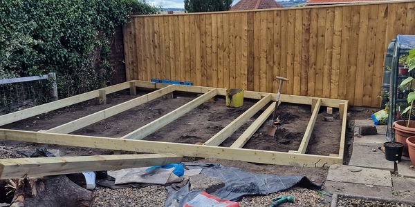 Wooden frame construction on bare soil in a backyard.