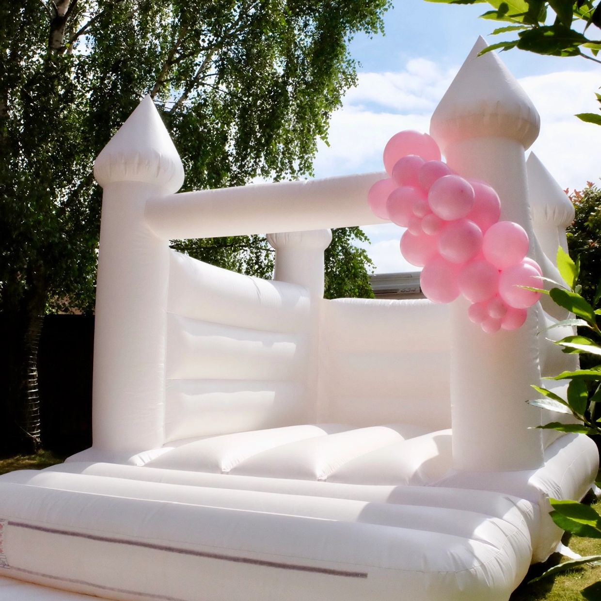 A white turret top bouncy castle in a garden with pink balloons for weddings and birthdays