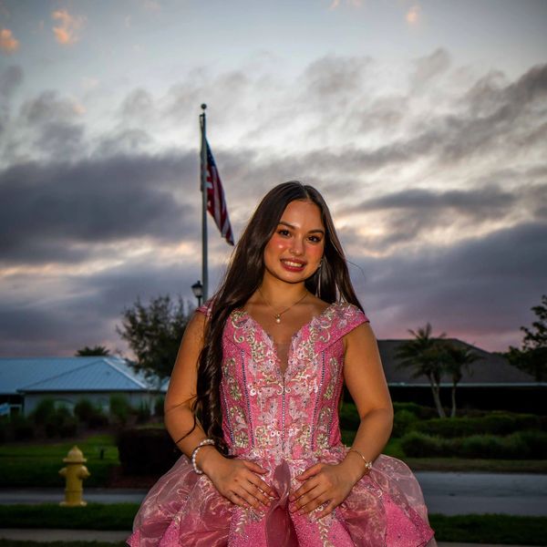 Young woman in an elegant pink dress posing outdoors at dusk.