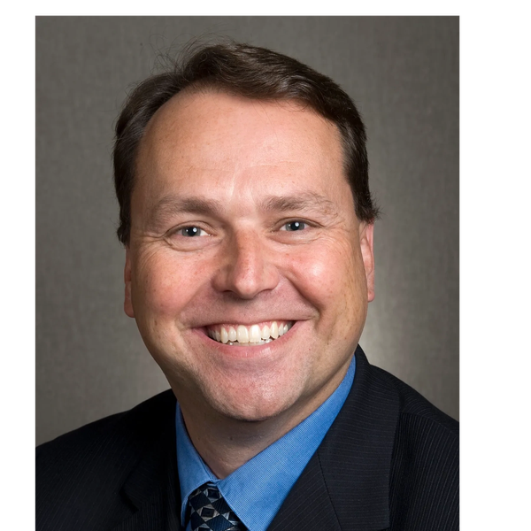 Smiling middle-aged man in business attire against a neutral background.