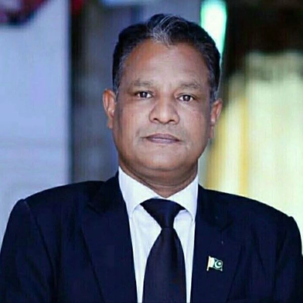 Man in a formal suit with a Pakistani flag pin on his lapel.