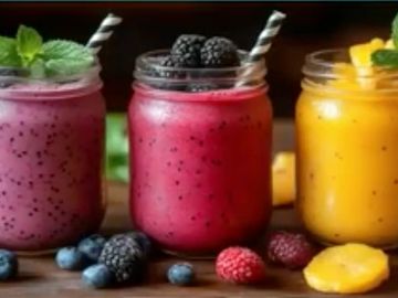 Three colorful fruit smoothies in jars with straws and fresh berries around.