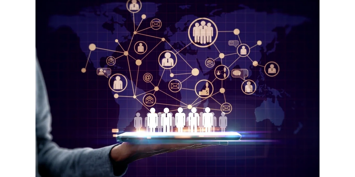 hand holding a tablet with cutouts of people standing on it, network of icons above it over a map