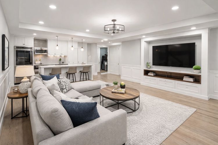 Modern open living room with light gray sectional and large TV.