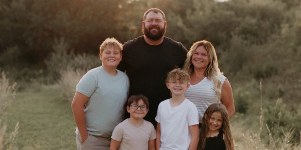 A happy family of six posing outdoors in the soft sunlight.