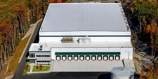 A large warehouse surrounded by colorful autumn trees near a lake.