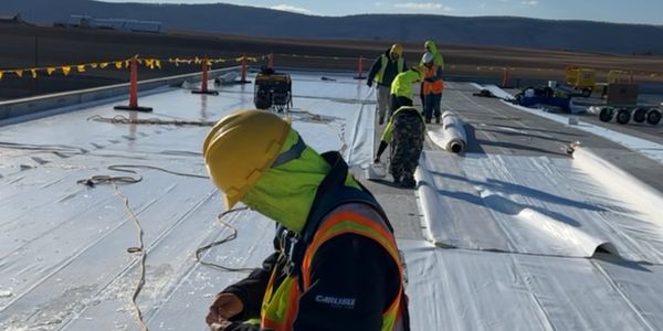 Workers installing roofing material under a clear sky with safety gear.
