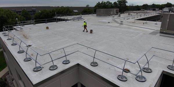 Worker inspects a flat rooftop with safety railings on a cloudy day.