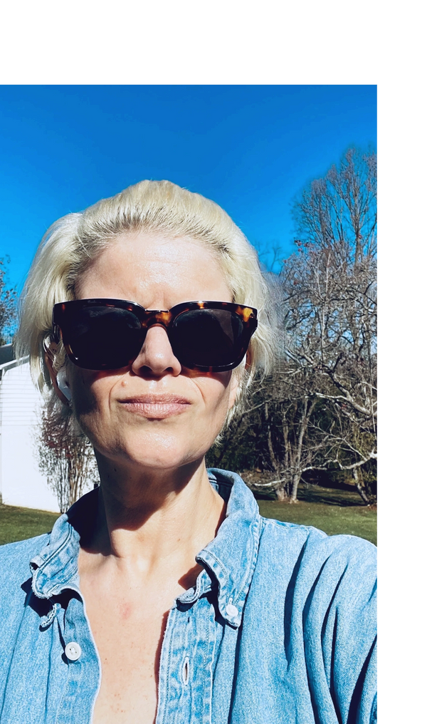 Woman with short blonde hair wearing sunglasses and a denim shirt outdoors on a sunny day.