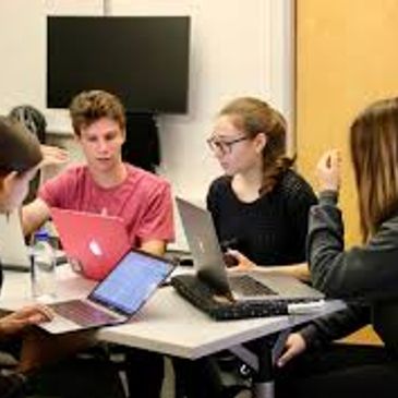 Four students collaborating with laptops at a table in a study session.