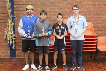 Four boys standing with trophies and medals in front of a brick wall.