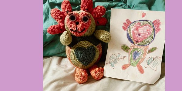 Crocheted doll beside a colorful child's drawing of the same figure.