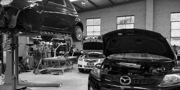Black and white photo of a busy auto repair garage with cars lifted and hoods open.
