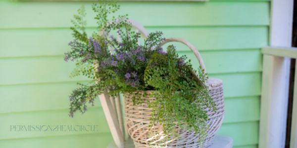 Wicker basket filled with greenery and purple flowers on a white chair.