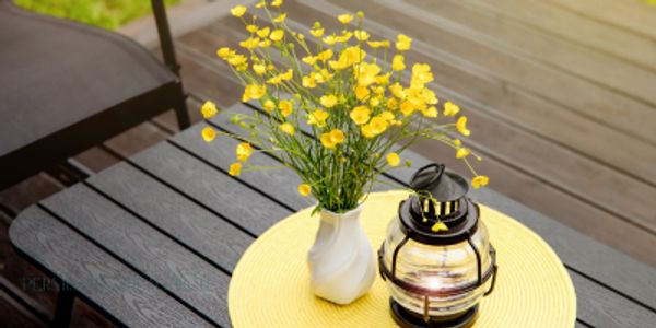 Yellow flowers in white vase and black lantern on table.