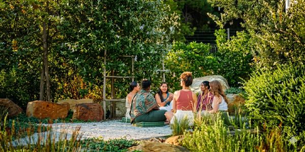 Group of friends sitting in a circle outdoors surrounded by greenery.