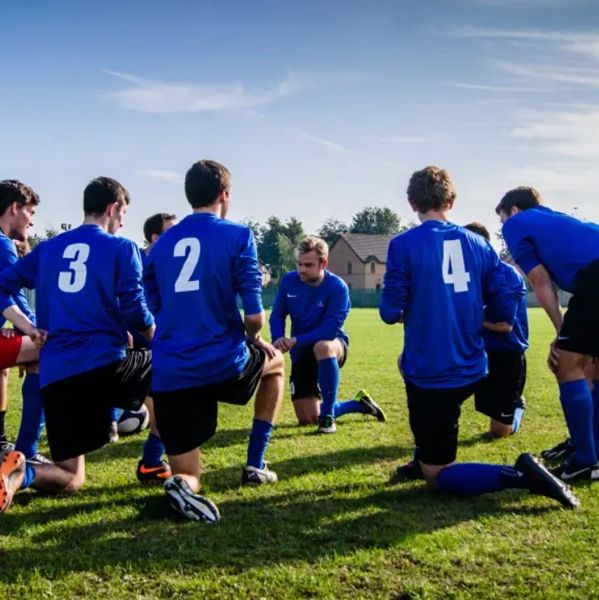 Soccer team in blue jerseys kneeling on the field during a discussion.