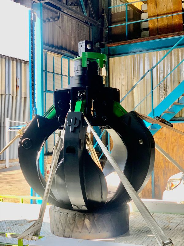 Industrial mechanical claw gripping a large metal cylinder inside a warehouse.