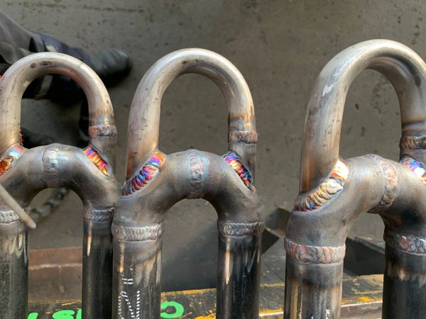 Close-up of metallic pipes with colorful weld joints arranged vertically.