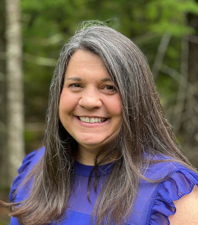 Smiling woman with long gray hair in a blue top outdoors.