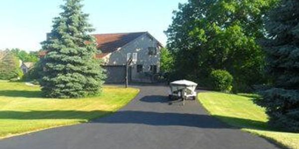 A suburban house with a freshly paved driveway and two large pine trees.