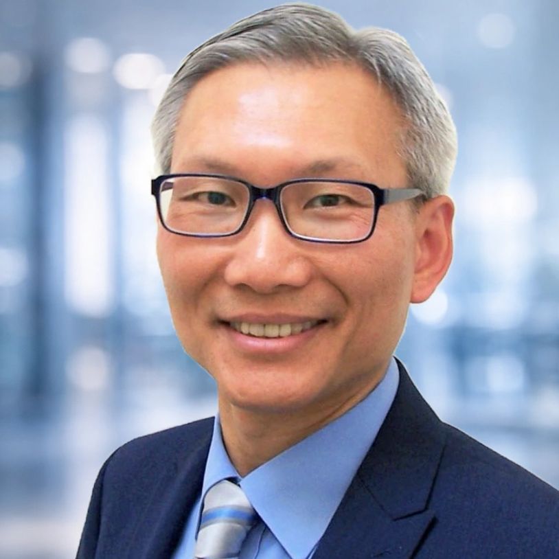 Smiling man in glasses and business suit with a blurred office background.