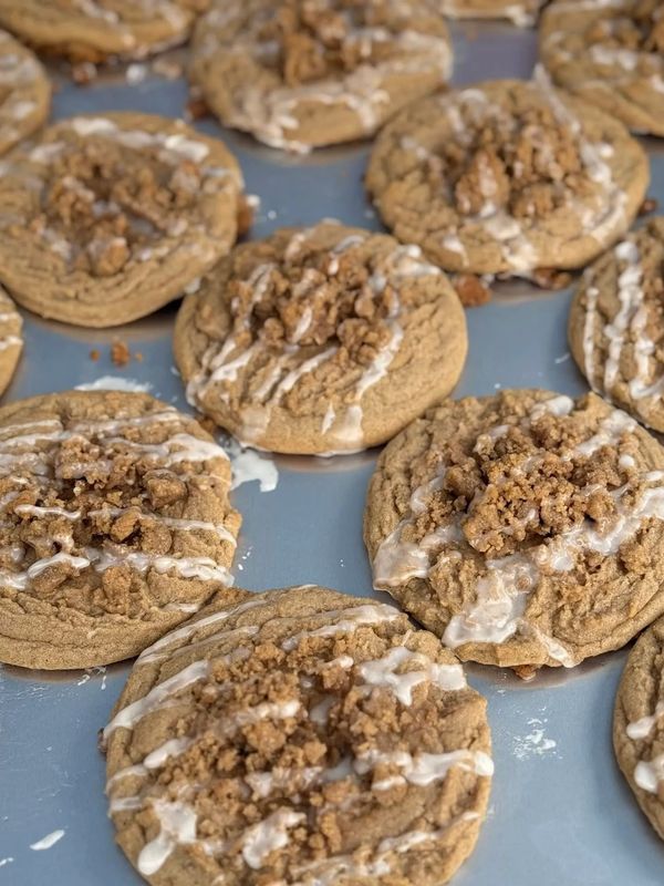 Freshly baked cookies with crumb topping and icing drizzle on a baking tray.