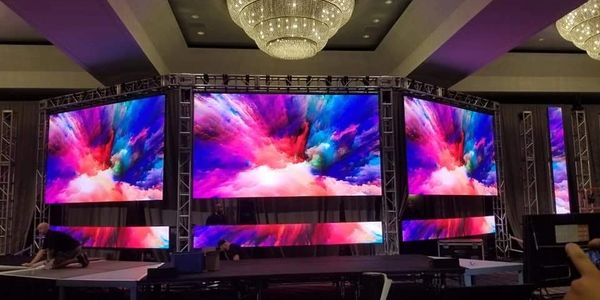Three large LED screens with vibrant, colorful visuals on a stage setup.
