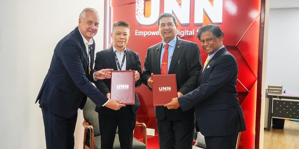 Four men in suits holding UNN folders and smiling in an office.