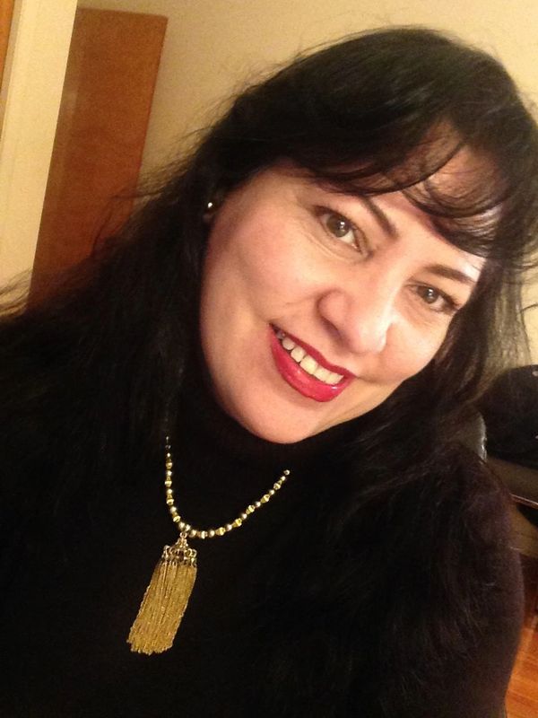Mujer sonriente con collar dorado y suéter oscuro.